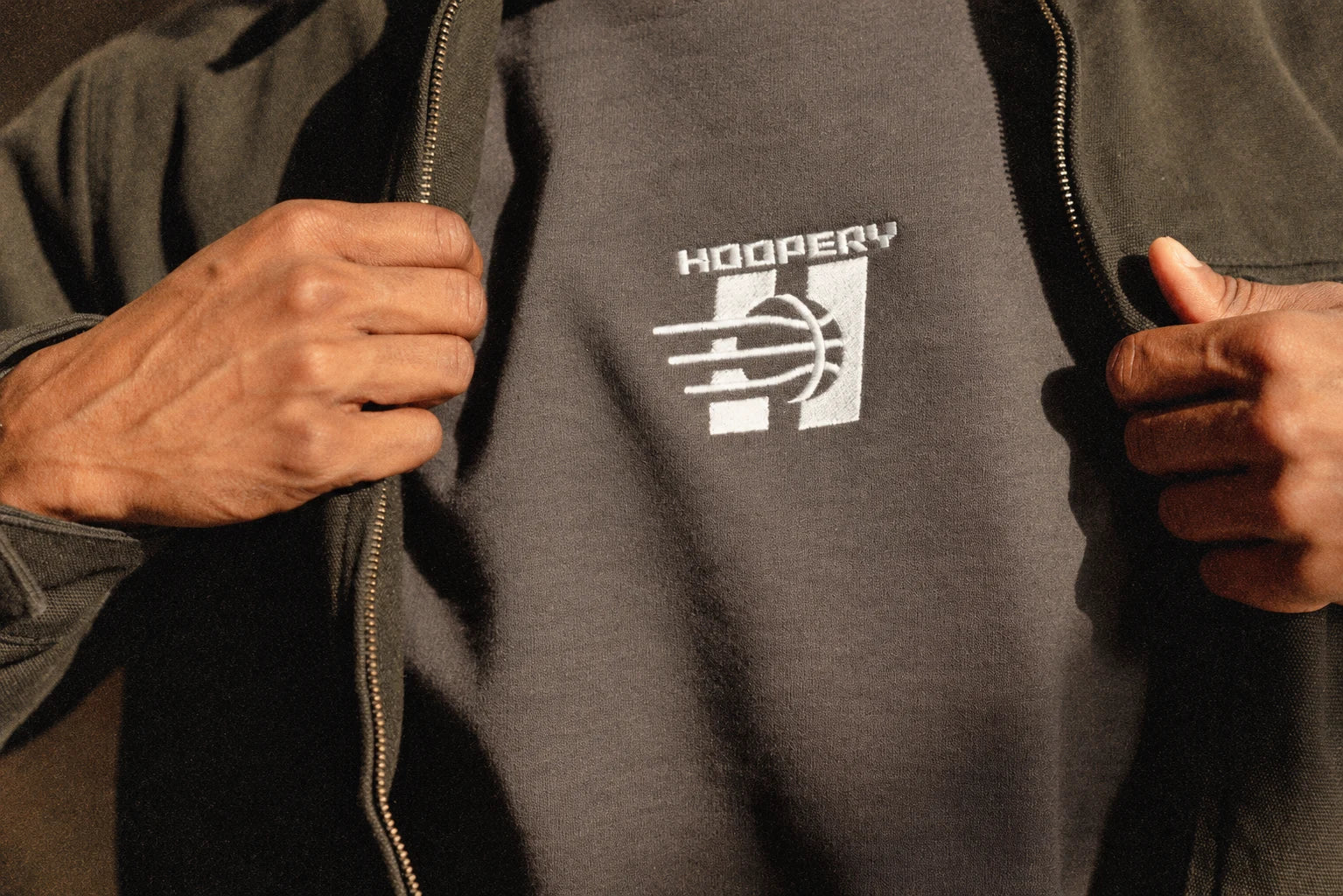Close-up of Hoopery embroidery on a gray shirt under a dark jacket