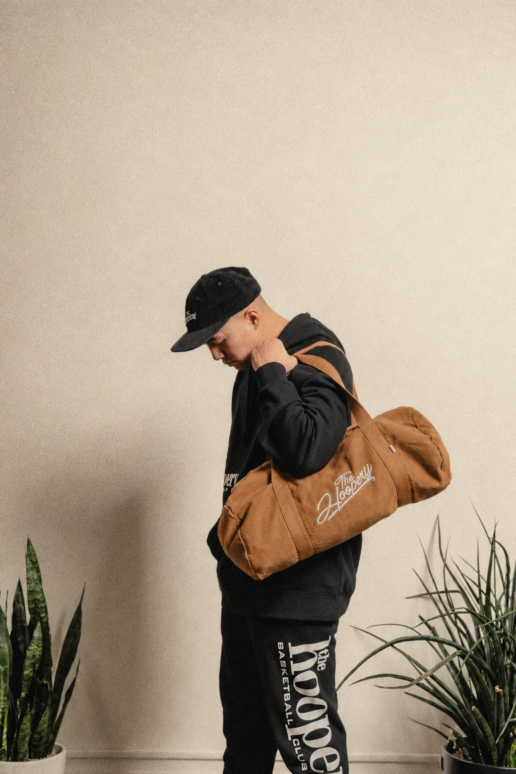 Model in black Hoopery clothing carrying a caramel duffel bag