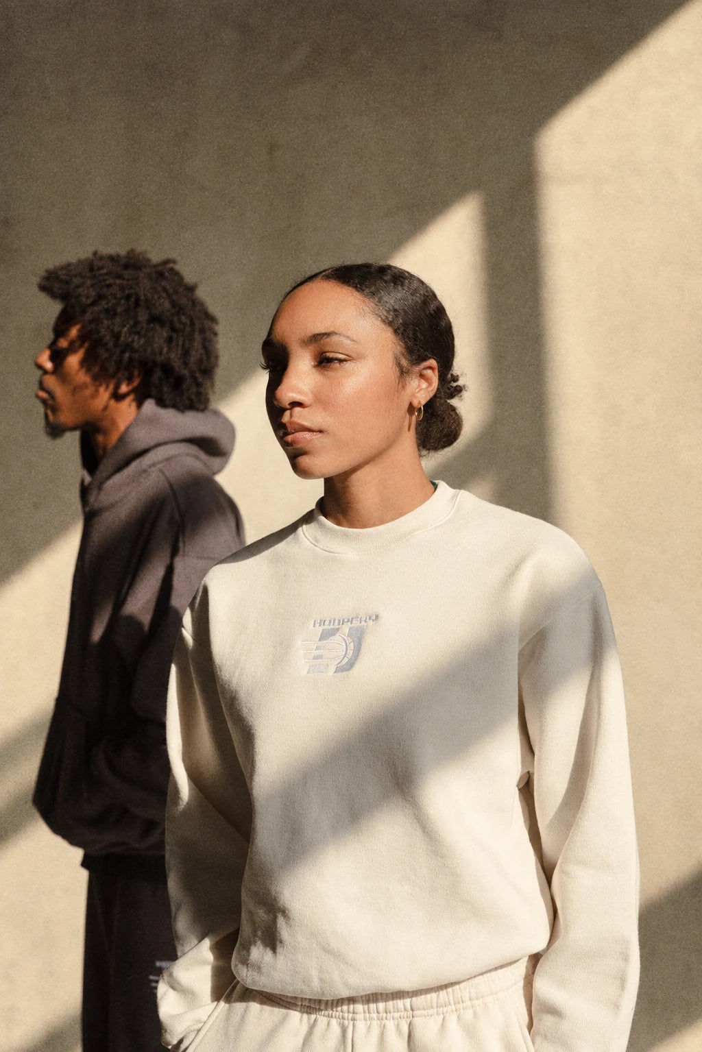 Two models wearing cream and charcoal Hoopery sweatshirts in sunlight